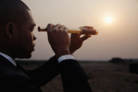 businessman-looking-through-spyglass-in-middle-of-the-desert